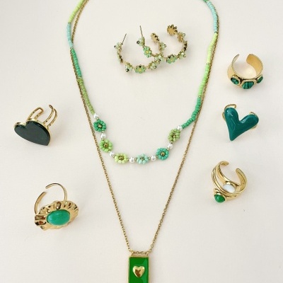 Conjunto de bijuterias com colares, brincos e anéis verdes e dourados sobre fundo branco.