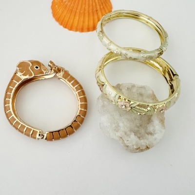 Três pulseiras douradas com design, elefante, pedra e concha laranja