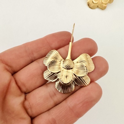 Brinco dourado em forma de flor segurado na mão