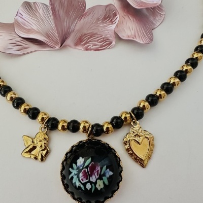 Colar com contas pretas e douradas e pendentes dourados com padrão floral no fundo branco