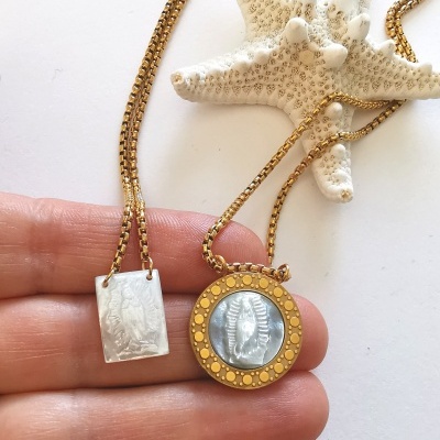 Duas correntes douradas com pendentes retangular prateado e redondo dourado com figura azul claro, sobre fundo branco e estrela-do-mar branca.