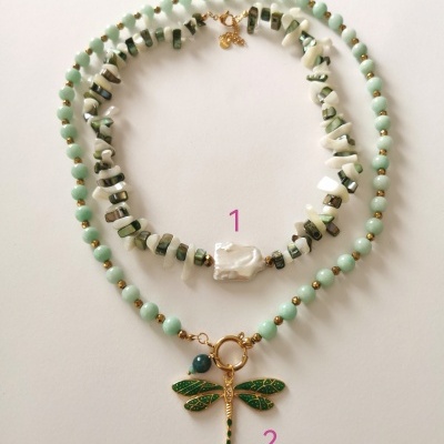 Dois colares sobre fundo branco, um de pedras irregulares brancas com detalhes verdes e outro de contas verdes com pendente de libélula dourado.