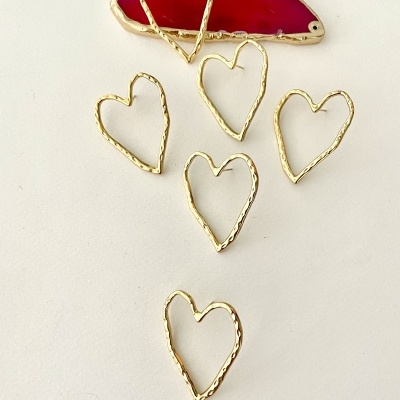 Pendentes em forma de coração dourados e peça vermelha com borda dourada sobre fundo branco