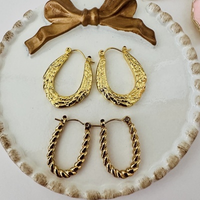 Brincos dourados texturizados em prato decorativo branco com laço dourado