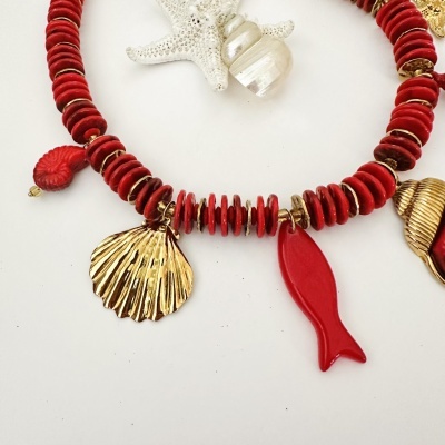 Colar com contas vermelhas e pendentes dourados e vermelhos sobre fundo branco com estrela-do-mar e concha