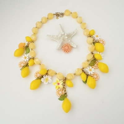 Colar com contas amarelas e pendentes de limões, flores e folhas sobre fundo branco com estrela-do-mar.