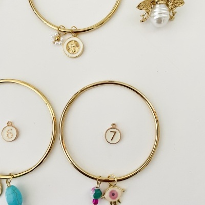 Brincos dourados com pendentes variados e etiquetas numeradas em fundo branco