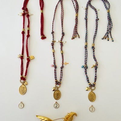 Três colares com medalhas e pingentes coloridos, e um broche dourado em forma de ave