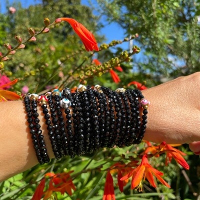 Pulseiras de contas pretas brilhantes num braço com flores vermelhas ao fundo