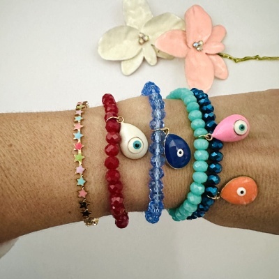 Pulseiras coloridas com contas e olhos pendurados no pulso com fundo de flores de tecido