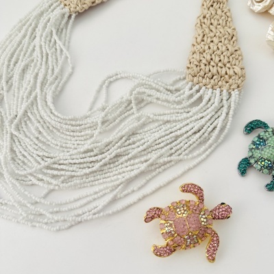 Colar de contas brancas com fecho em crochet bege e dois pins de tartaruga com pedras coloridas