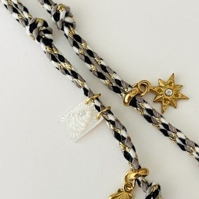 Colares com cordão trançado preto, branco e dourado com pendentes metálicos dourados variados.