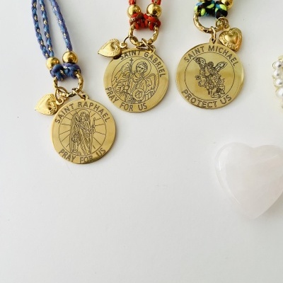 Pulseiras com medalhões dourados de santos e cordões trançados coloridos