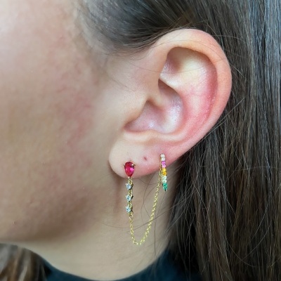 Brincos dourados com pedras coloridas e corrente na orelha de mulher