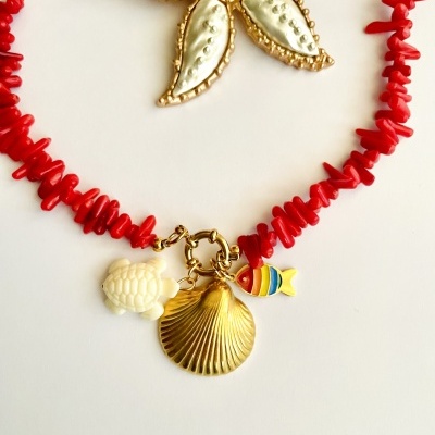 Colar com contas vermelhas e pingentes coloridos e dourados sobre fundo branco e flor dourada