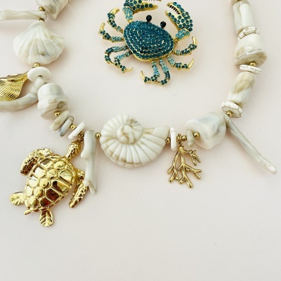 Colar com pendentes marinhos dourados e conchas brancas junto a broche de caranguejo azul