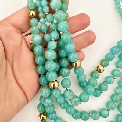 Colar verde água com esferas metálicas douradas segurado por mão
