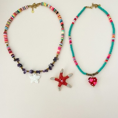 Dois colares coloridos com pendentes de estrela do mar branca e coração vermelho, junto de um broche estrela do mar vermelho