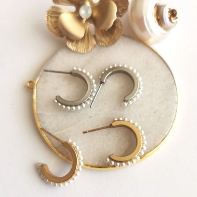 Dois pares de brincos meia argola com pérolas sobre prato branco com borda dourada e decoração com flor dourada e concha