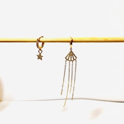 Dois brincos de metal dourado pendurados num pau fino de madeira claro