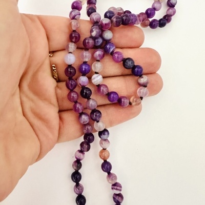 Colar ou pulseira de contas roxas segurado por uma mão