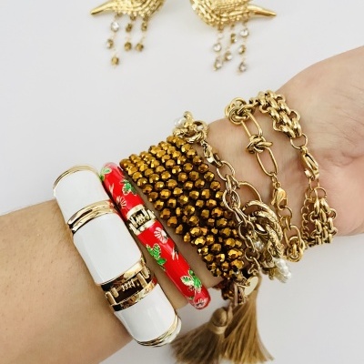 Braço com várias pulseiras douradas, branca e vermelha e brincos dourados de pássaros