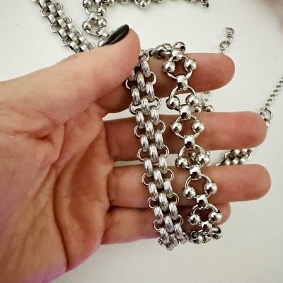Colares prateados metálicos com texturas distintas segurados por mão