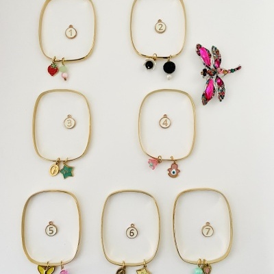 Sete pulseiras douradas com pingentes coloridos numeradas de 1 a 7 sobre fundo branco