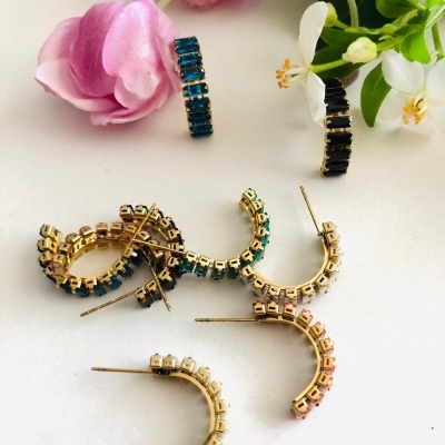 Brincos argola dourados com pedras coloridas perto de flores cor de rosa e brancas