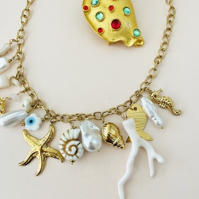 Colar dourado com pendentes de conchas e coral ao lado de alfinete dourado com pedras coloridas