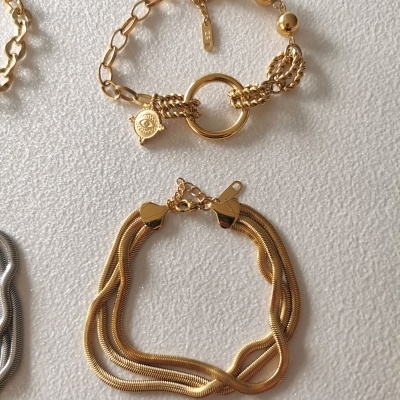 Duas pulseiras douradas de formatos distintos sobre fundo branco