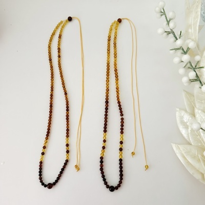 Duas pulseiras ou colares amarelos e castanhos com fio amarelo sobre fundo branco com decoração branca ao lado.