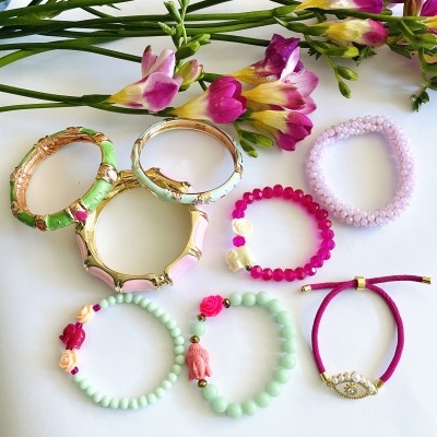 Pulseiras coloridas com contas e flores, sobre fundo branco com flores frescas roxas e amarelas