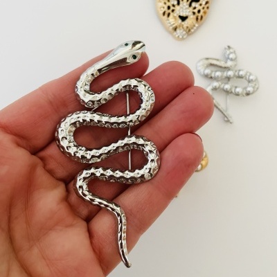 Alfinete prateado serpente na mão com alfinetes ao fundo