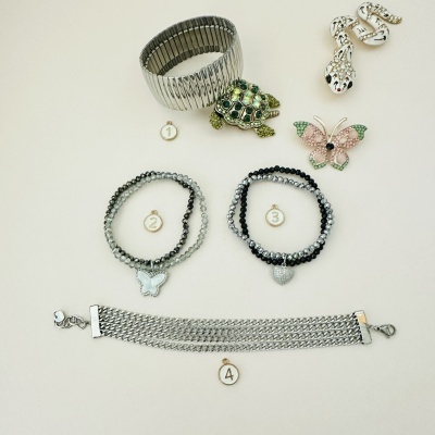 Conjunto de pulseiras e brincos em metal prateado e contas, incluindo tartaruga e borboletas, sobre fundo branco