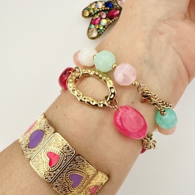 Bracelete dourada com corações coloridos e pulseira de pedras coloridas em pulso sobre fundo branco