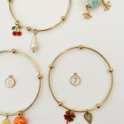 Três pulseiras douradas com pingentes coloridos e uma figura de rã azul com detalhes dourados