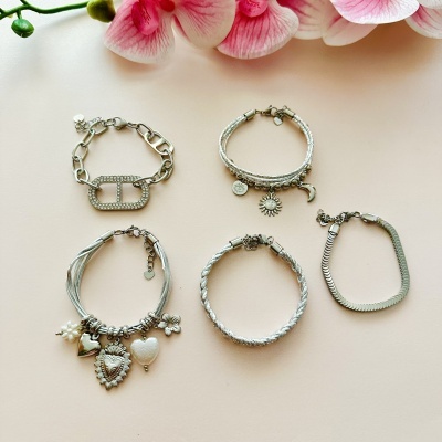 Cinco pulseiras prateadas com pendentes e orquídea rosa sobre fundo bege