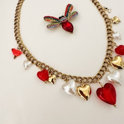 Colar dourado com pendentes de corações e pássaro, e broche colorido em forma de libélula.
