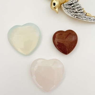 Três pedras em forma de coração e um broche de pássaro próximo.