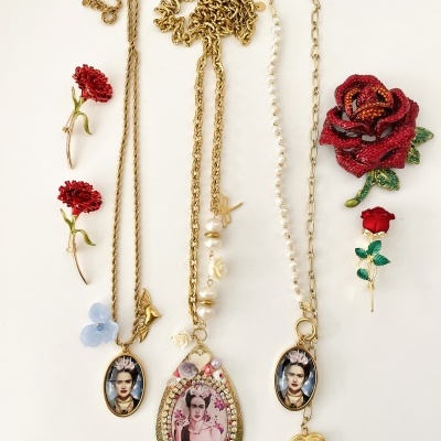 Três colares com pendentes dourados e fotografias femininas junto a seis broches de flores sobre fundo branco