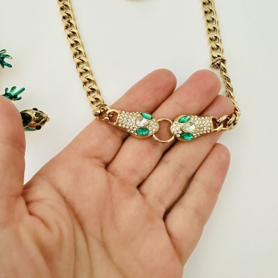 Colar dourado com pedras verdes e transparentes em fundo branco