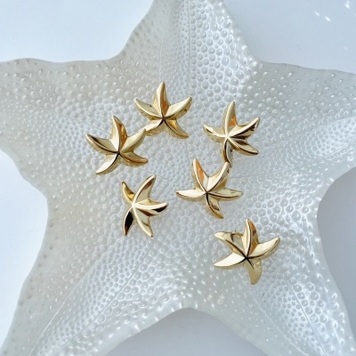 Brincos dourados em forma de estrelas do mar sobre estrela do mar decorativa branca.