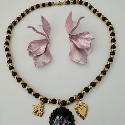 Colar com contas douradas e pretas com pendentes e brincos rosa em fundo branco