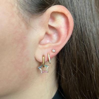 Orelha com três brincos dourados, incluindo uma estrela colorida pendente