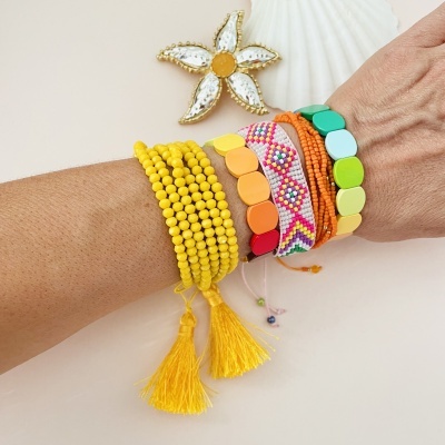Pulseiras coloridas em vários materiais em braço com concha e estrela do mar ao fundo