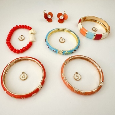 Conjunto de bijuterias vibrantes com pulseiras e brincos em tons vermelhos, brancos, azuis e laranja sobre fundo branco.