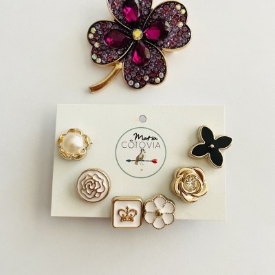 Broches decorativos florais e de trevo com pedras roxas e detalhes dourados em cartão branco