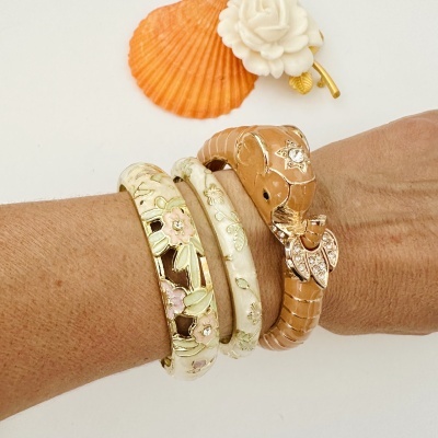 Três pulseiras douradas com flores e crocodilo em esmalte, usadas no pulso