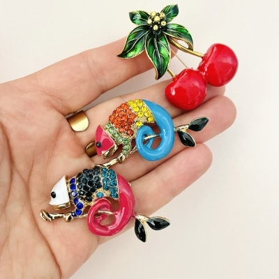 Broches esmaltados coloridos de cerejas e camaleões na mão